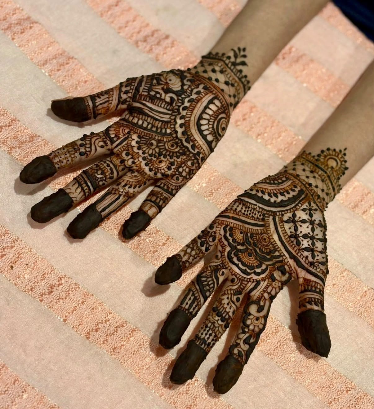 Detailed paisley and floral henna on two palms against a peach towel